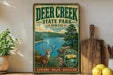A vintage-style metal sign for Deer Creek State Park in Ohio, featuring a scenic illustration of a deer in a wooded area with a lake and mountains in the background.