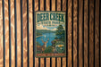 A vintage metal sign for Deer Creek State Park in Ohio, featuring an illustration of a deer and a lake surrounded by trees.