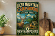 A vintage-style sign for Deer Mountain Campground in New Hampshire, featuring a deer in a forest setting with a campfire and tents.