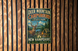 A metal sign for Deer Mountain Campground in New Hampshire, featuring a deer and camping tents in a scenic outdoor setting.