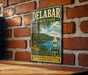 A vintage-style metal sign for Delabar State Park, featuring a scenic landscape with a lake, sailboat, and lush greenery.