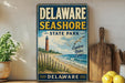 A vintage metal sign for Delaware Shore State Park, featuring a lighthouse and beach scene, is displayed on a shelf next to a wooden cutting board and a potted plant.