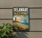 A vintage metal sign for Delaware Shore State Park, featuring a lighthouse and beach scene, is displayed on a wall next to a plant.