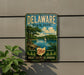 A vintage metal sign for Delaware State Park, featuring a scenic landscape with a lake, trees, and a sailboat.