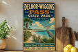 A vintage-style sign for Delnor-Wiggs Pass State Park in Florida, featuring a beach scene with palm trees, a heron, and a wooden walkway leading to the beach.
