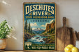 A vintage-style metal sign advertising Deschutes River State Recreation Area in Oregon, featuring a scenic mountain landscape with a river flowing through it.