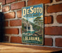A vintage-style metal sign for Desoto State Park in Alabama, featuring a scenic illustration of a waterfall and forest.