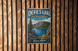 A vintage metal sign for Devil's Lake, Oregon, featuring a scenic landscape with a lake, mountains, and pine trees.