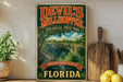 A vintage-style sign for Devil's Millhopper Geological State Park in Florida, featuring a scenic image of the park's natural landscape.