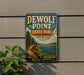A vintage-style metal sign for DEWOLF POINT STATE PARK, NEW YORK, featuring a scenic landscape with a path leading to a body of water.