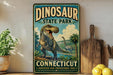A vintage-style sign for Dinosaur State Park in Connecticut, featuring a T-Rex dinosaur and tropical landscape.
