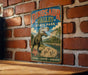 A vintage-style metal sign for Dinosaur Valley State Park, featuring a large illustration of a T-Rex dinosaur and a scenic landscape.