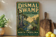 a vintage-style sign for DisMAL SWAMP STATE PARK in North Carolina, with a bird illustration and a natural landscape.