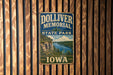 A vintage metal sign for Dolliver Memorial State Park in Iowa, featuring a scenic landscape with a river and mountains.