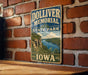 A vintage metal sign for the Doliver Memorial State Park in Iowa, featuring a scenic landscape with a river and mountains.