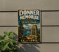 A vintage metal sign for Donner Memorial State Park in California, featuring a scenic landscape with mountains, trees, and a monument.