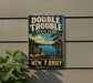 A vintage metal sign for Double Trouble State Park in New Jersey, featuring a scenic landscape with a lake and pine trees.