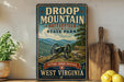 a vintage-style sign for Droop Mountain Battlefield State Park in West Virginia, with a cannon and mountains in the background.