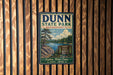 A vintage metal sign for Dunn State Park in Massachusetts, featuring a scenic landscape with a lake and pine trees.
