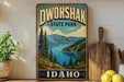 A vintage-style sign for Dworshak State Park in Idaho, featuring a scenic landscape with pine trees, mountains, and a lake.