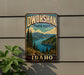 A vintage-style metal sign for Dworshak State Park in Idaho, featuring a scenic landscape with pine trees, mountains, and a lake.