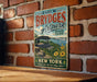 A vintage-style metal sign for "Brydges Artpark" in New York, featuring a scenic illustration of the park and its surroundings.