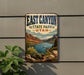 A vintage-style sign for East Canyon State Park in Utah, featuring a scenic landscape with mountains, a lake, and a boat on the water.