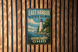 A vintage-style metal sign for East Harbor State Park in Ohio, featuring a lighthouse and a scenic landscape.