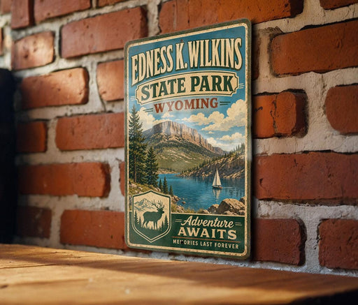 A vintage-style metal sign for Edness K. Wilkins State Park in Wyoming, featuring a scenic mountain landscape with a lake and a sailboat.