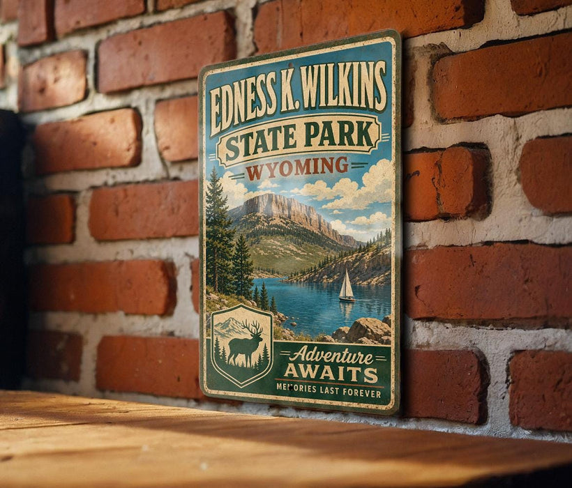 A vintage-style metal sign for Edness K. Wilkins State Park in Wyoming, featuring a scenic mountain landscape with a lake and a sailboat.
