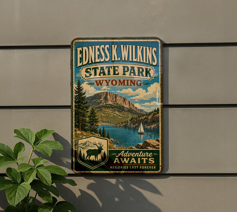 A vintage-style metal sign for Edness K. Wilkins State Park in Wyoming, featuring a scenic mountain landscape with a lake and a sailboat.