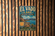 A vintage metal sign for El Vado Lake State Park, featuring a scenic landscape with mountains, water, and a boat, mounted on a wooden wall.