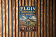 A vintage-style metal sign for Elgin Schoolhouse, a historic site in Nevada, is displayed on a wooden wall.
