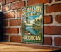 A vintage metal sign for Eljah Clark State Park in Georgia, featuring a scenic landscape with a river and trees.