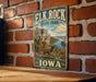 A vintage-style metal sign for Elk Rock State Park in Iowa, featuring a scenic landscape with a river, cliffs, and wildlife.
