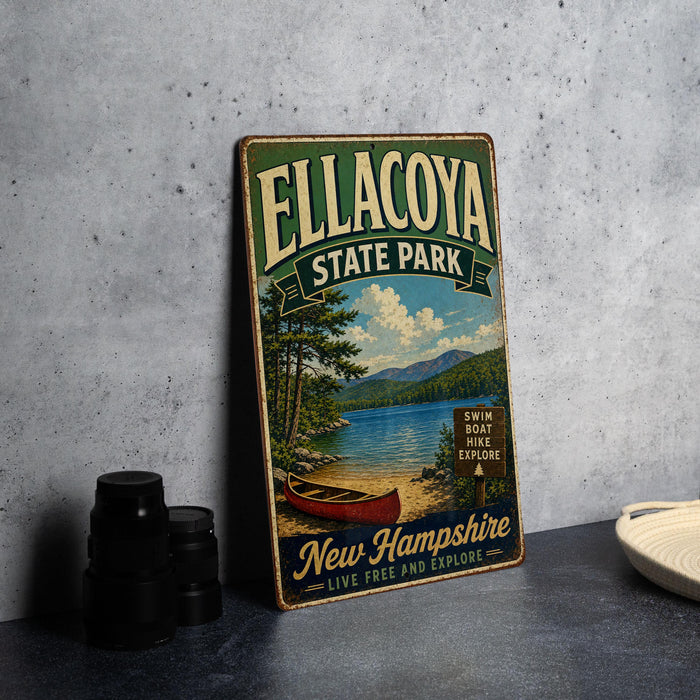 A vintage metal sign for Ellacoya State Park, featuring a scenic image of a lake and mountains, is displayed on a gray countertop next to a stack of black camera lenses.