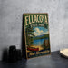 A vintage metal sign for Ellacoya State Park, featuring a scenic image of a lake and mountains, is displayed on a gray countertop next to a stack of black camera lenses.