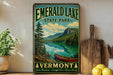 A vintage-style sign for Emerald Lake State Park in Vermont, featuring a scenic landscape with a lake, mountains, and a canoe.