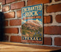 A vintage-style sign for the Enchanted Rock State Natural Area in Texas, featuring a mountain landscape with a desert and cactus in the background.