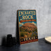 A vintage-style metal sign for Enchanted Rock, a state natural area in Texas, featuring a desert landscape with a large rock formation and desert plants.