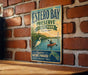 A vintage-style sign for Estero Bay Preserve, Florida, featuring a scenic illustration of a person kayaking in a river with a lighthouse in the background.
