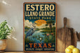 A vintage-style metal sign for Estero Llanos Grande State Park, featuring a blue heron, palm trees, and a sunset landscape.