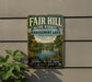 a vintage metal sign with a scenic landscape, including a lake, trees, and a bird, mounted on a wall.