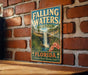 A vintage-style sign for Falling Waters State Park in Florida, featuring a waterfall and tropical foliage, is displayed on a brick wall.