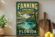 A vintage-style sign for Fannin Springs State Park in Florida, featuring a scenic image of a river surrounded by lush greenery and a wooden bridge.