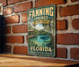 A vintage-style metal sign for Fannin Springs State Park in Florida, featuring a scenic image of a pond surrounded by lush greenery.