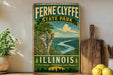 A vintage-style sign for Fernne Clyde State Park in Illinois, featuring a scenic landscape with a river and mountains.