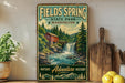 A vintage-style sign for Fields Spring State Park in Washington, featuring a waterfall and a red barn, is displayed on a wall next to a wooden cutting board and some potted plants.