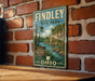 A vintage metal sign for Findley State Park in Ohio, featuring a scenic landscape with a lake and mountains.