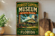 A vintage-style sign for the Forest Capital Museum in Florida, featuring an illustration of a wooden cabin and a wagon, with the text "A Slice of Florida's History" and "State Park".